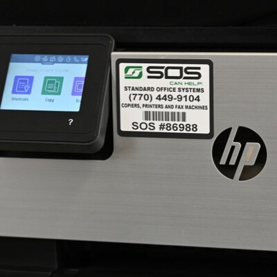 A rectangular sticker with a barcode on a printer with the company information and an ID number