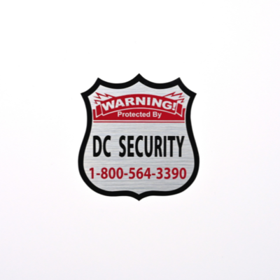 A silver badge sticker with a black border and black and red text that reads 'Warning protected by DC Security'
