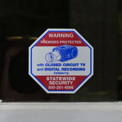 A red, white, and blue octagonal sticker that warns of CCTV cameras protecting the property.