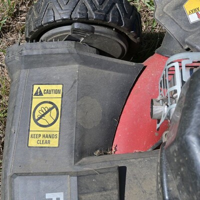 A yellow rectangular caution keep hands clear sticker on a lawnmower
