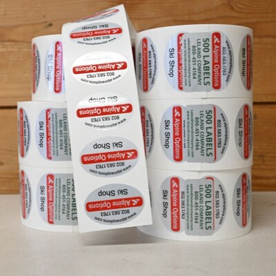 Six rolls of labels stacked on a table, they are grey, red, and black